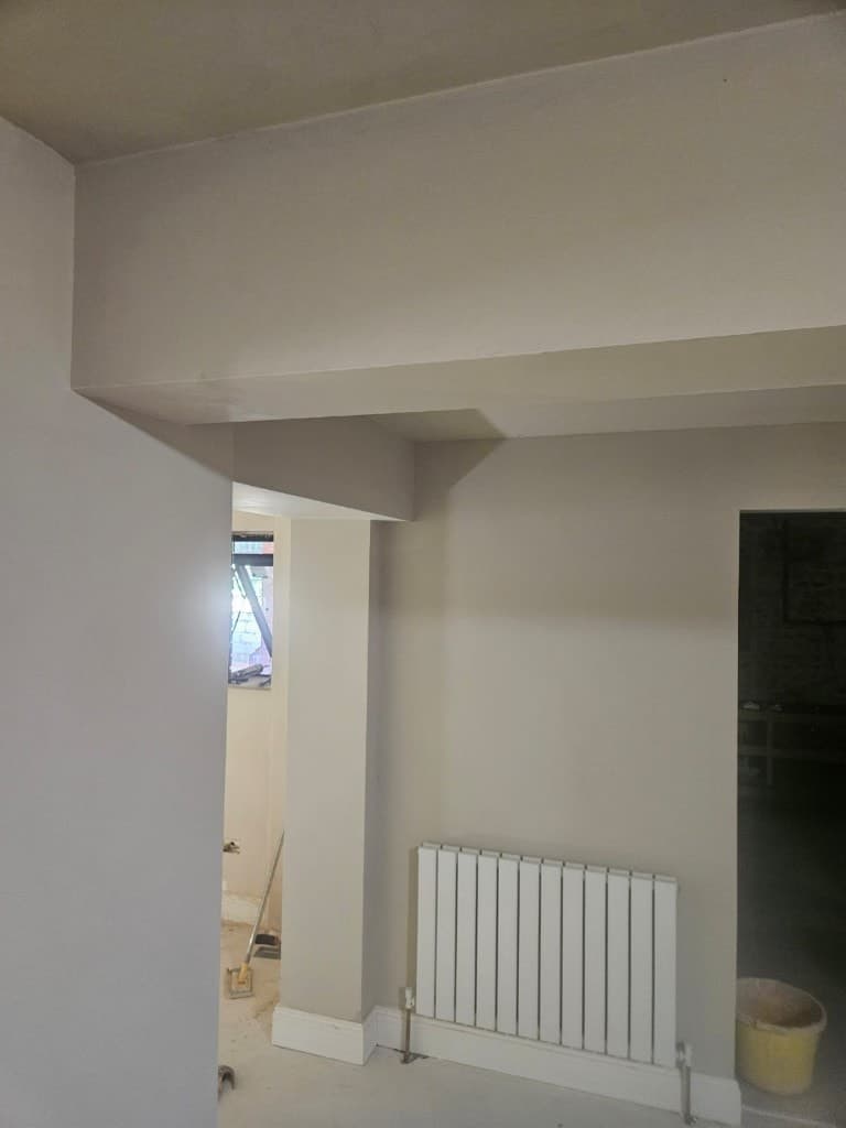 Freshly painted cream interior with a white radiator, ceiling bulkhead and protective floor coverings during a painting job.