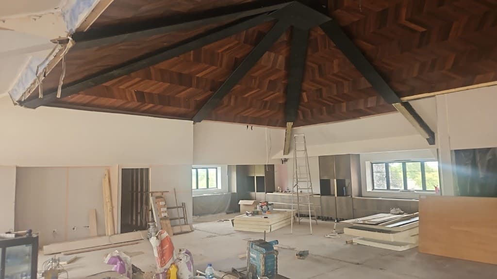 Vaulted herringbone wood ceiling with black beams, off-white walls, dark cabinetry and decorating equipment during an interior fit-out.
