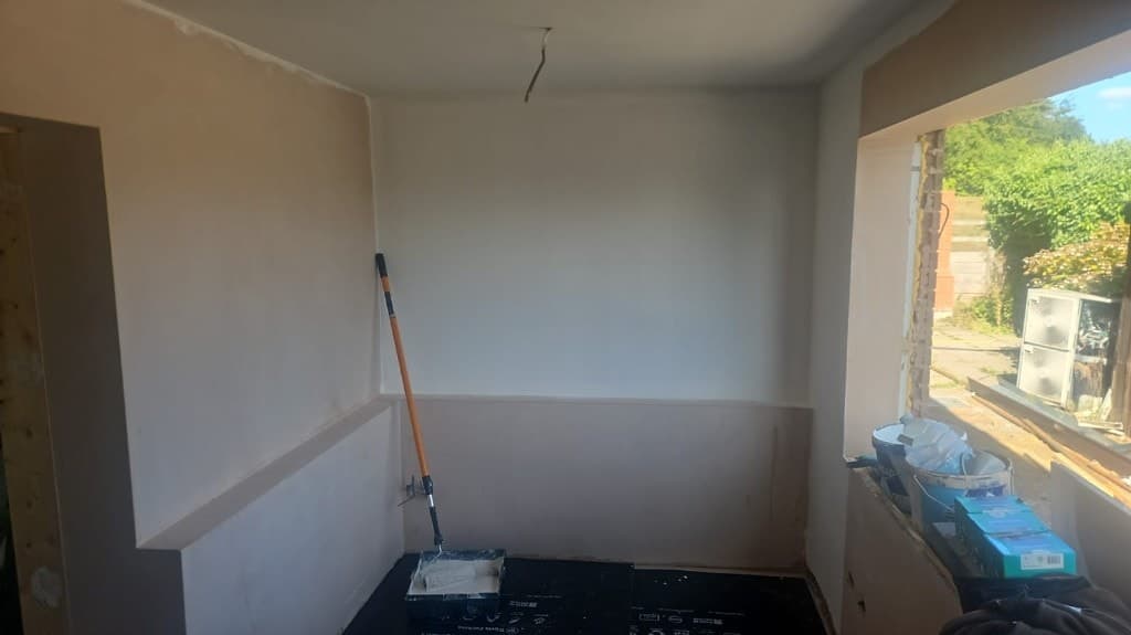 Interior room in preparation with freshly plastered walls, white primer, black floor protection and a roller on an extension pole.