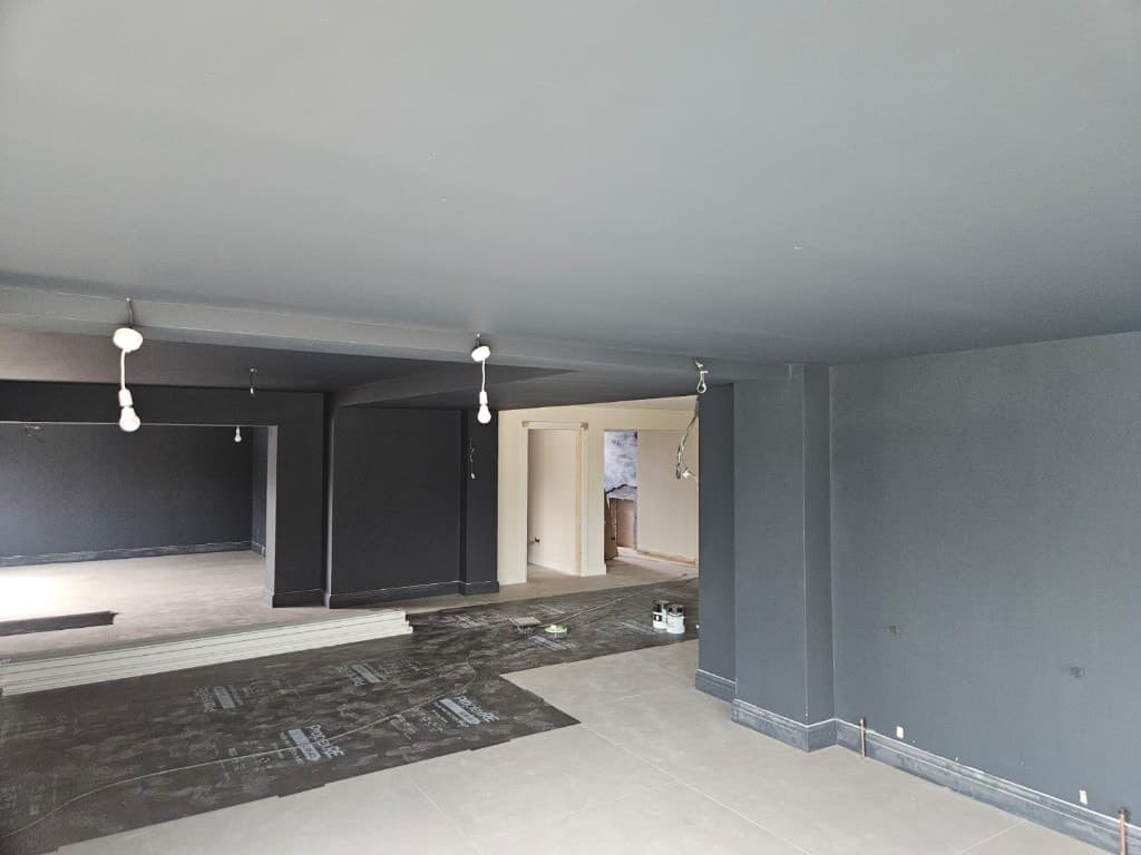Open-plan interior with charcoal grey colour-drench paint on walls and ceiling, protective floor covering and temporary lighting.