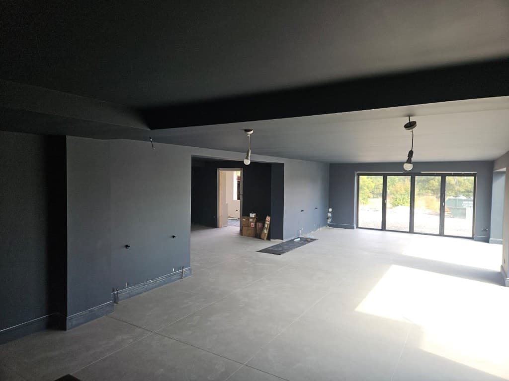 Charcoal grey colour-drenched living space with light grey floor tiles, hanging work lights and black-framed bi-fold doors.
