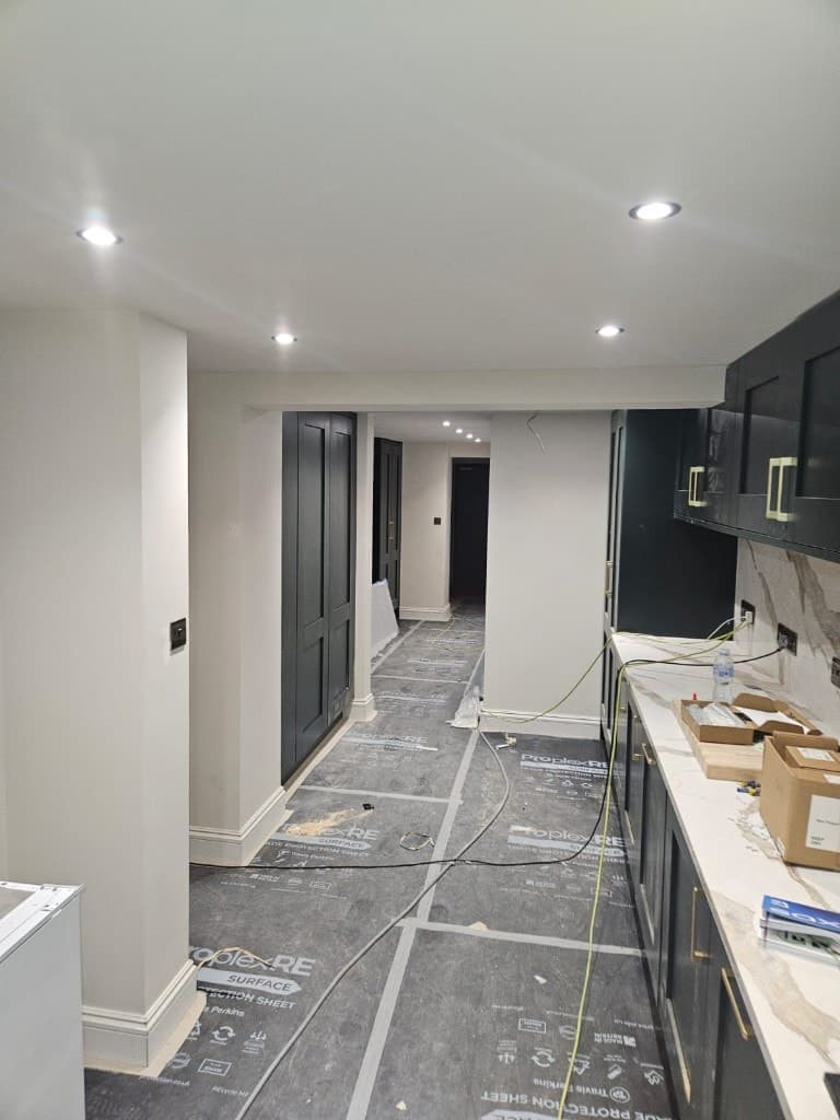 Kitchen renovation in progress with cream walls, dark charcoal cabinets with gold handles, marble-effect worktops and protected flooring.
