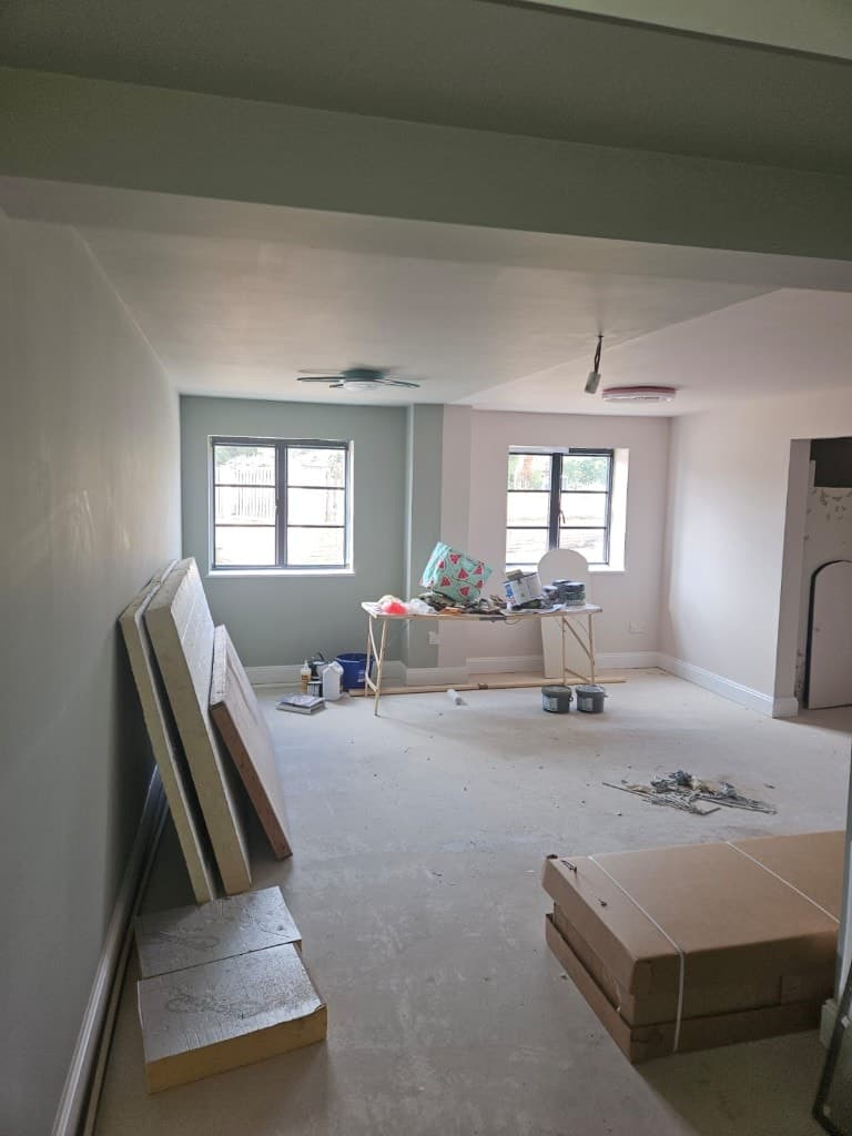 Large room with pale sage green and cream walls, black-framed windows and painting supplies set out on a trestle table.