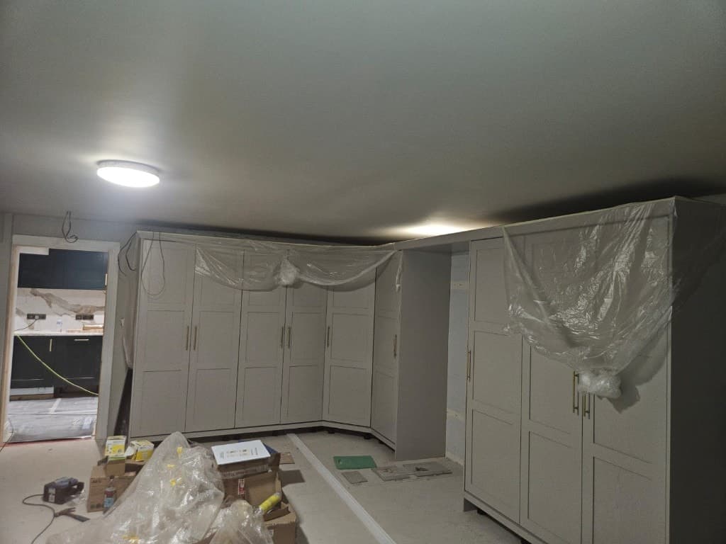 Floor-to-ceiling light grey fitted wardrobes with gold handles, protective sheeting and floor coverings during an interior decorating job.