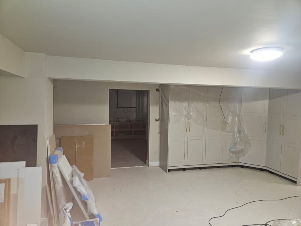 Newly installed white Shaker-style fitted wardrobes with brass handles in a freshly painted cream room.